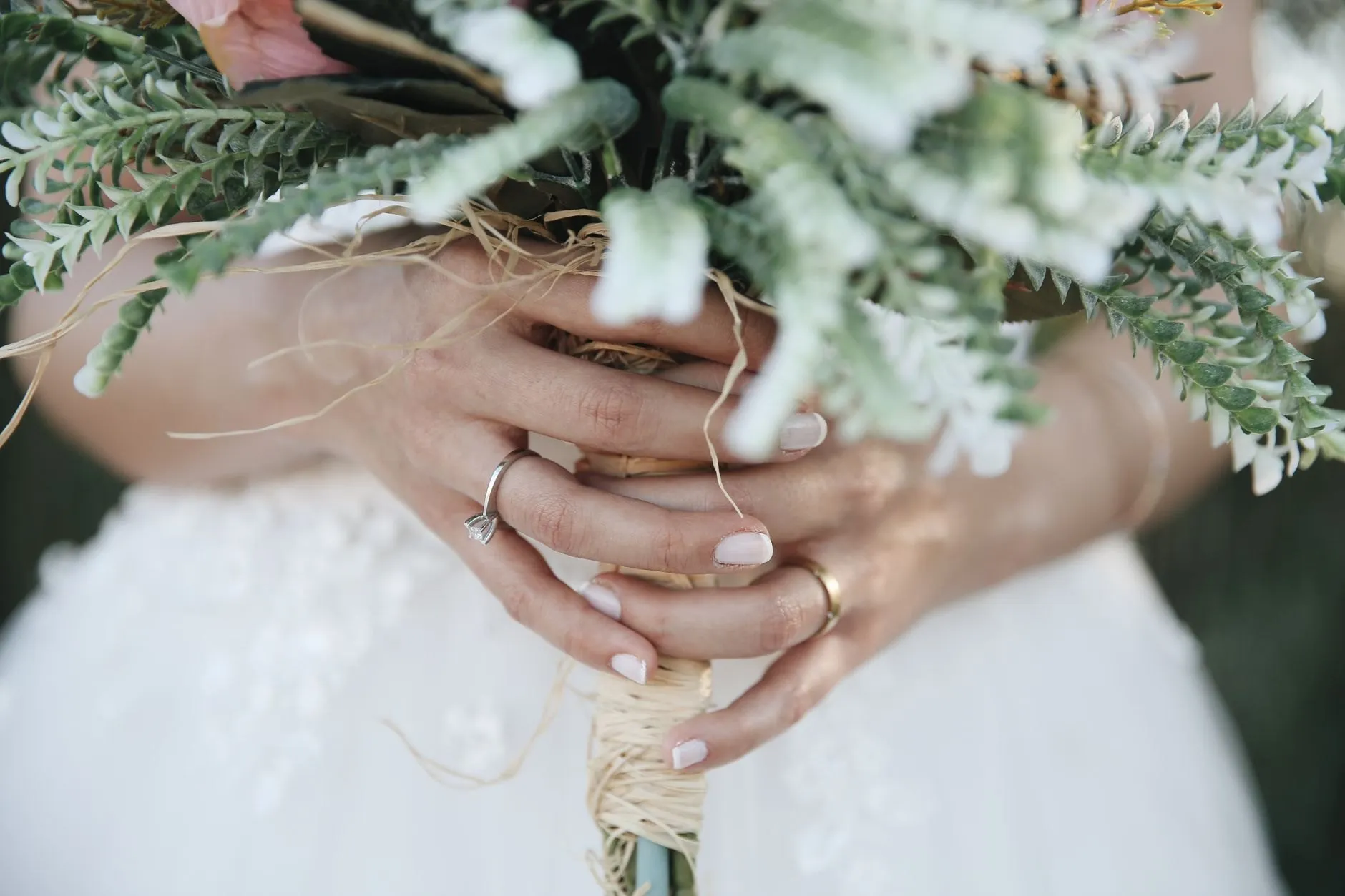Hands with wedding rings holding a bouquet of silver foliage