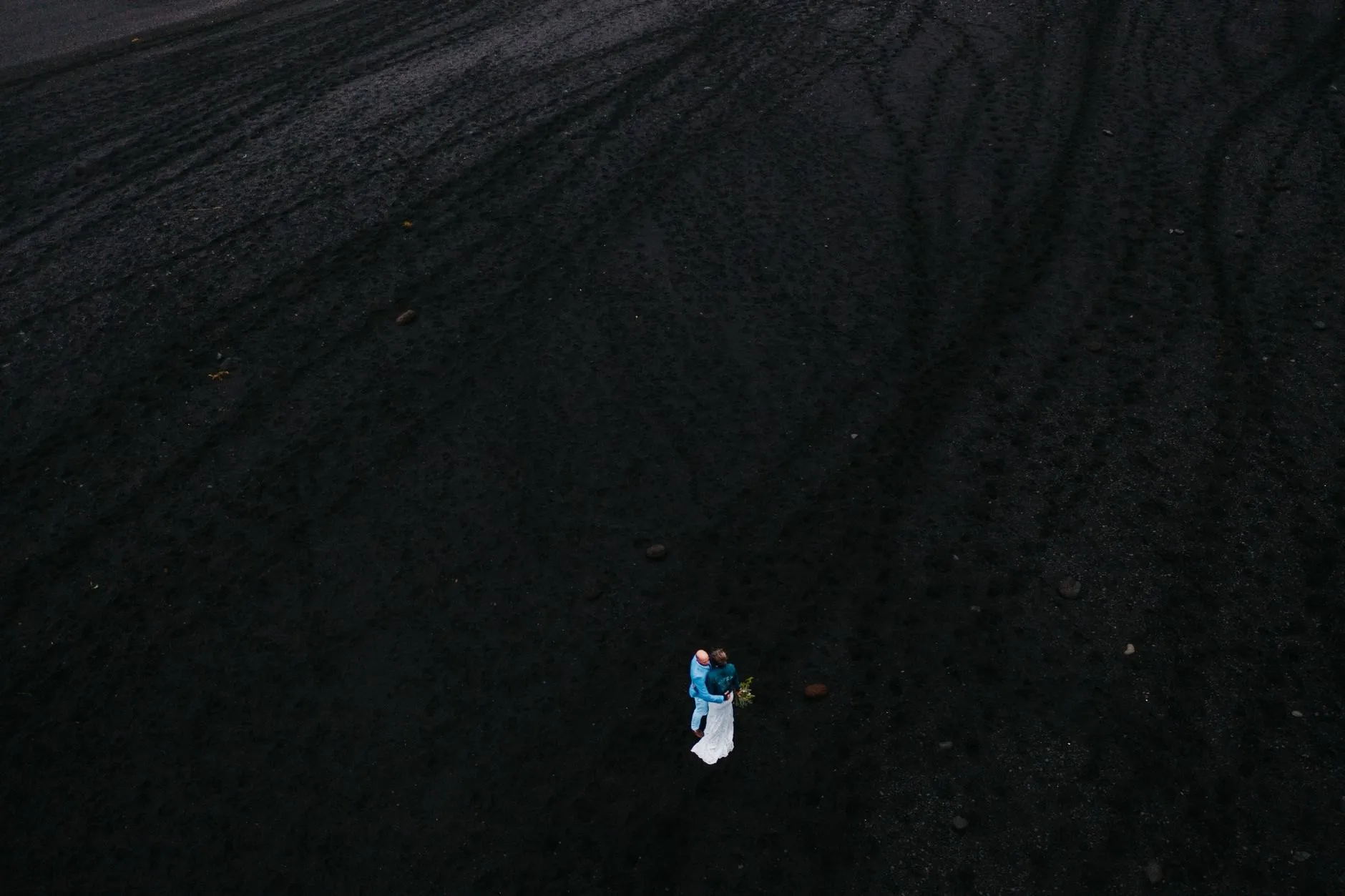 A couple alone on a black sand beach, seen from above
