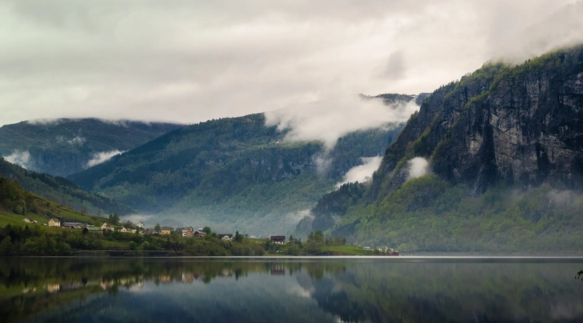 Mist on the steep sides of a Norwegian valley above a still lake and a few farmhouses