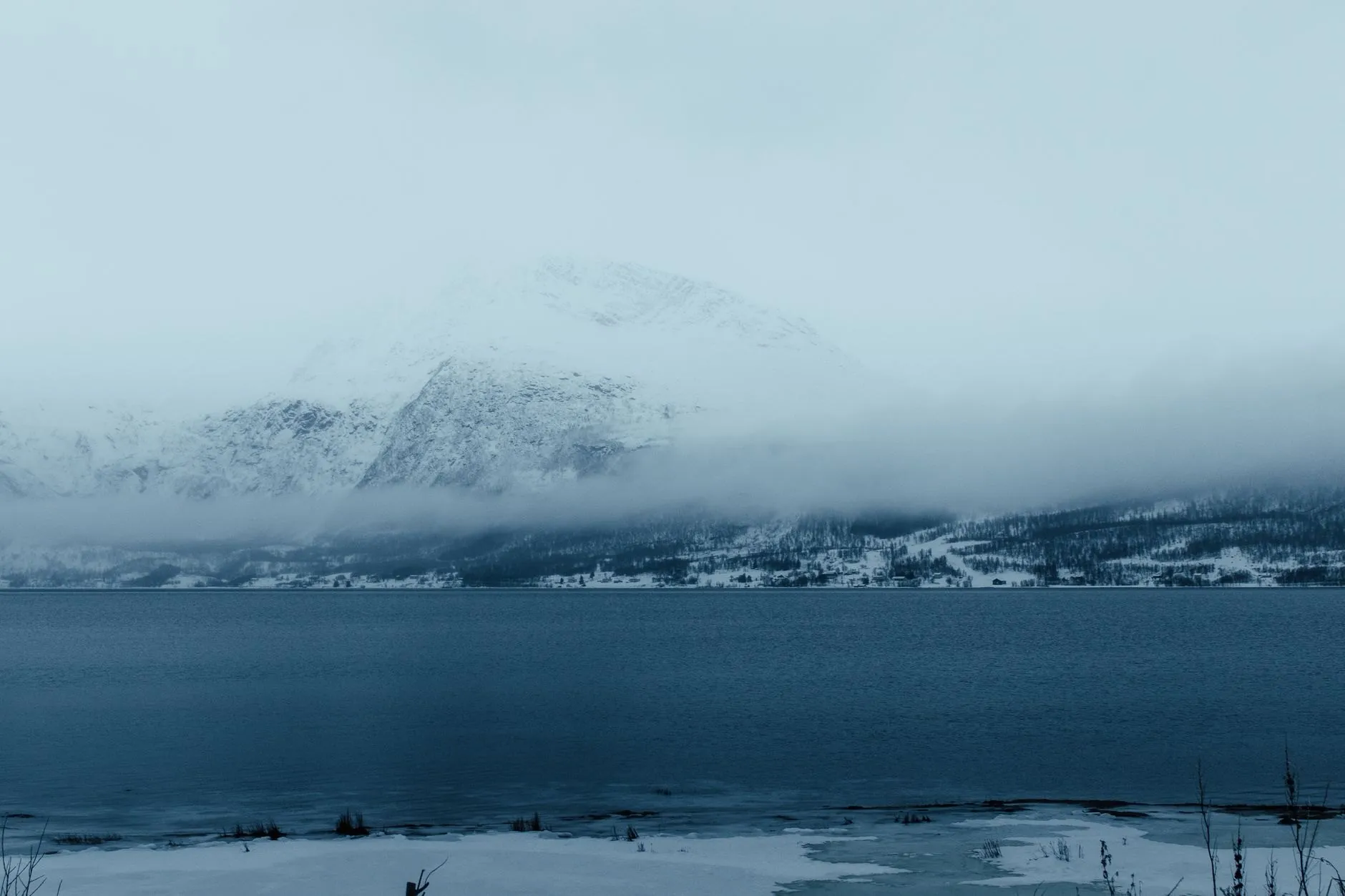 Snow-covered mountains half hidden in cloud above a winter lake