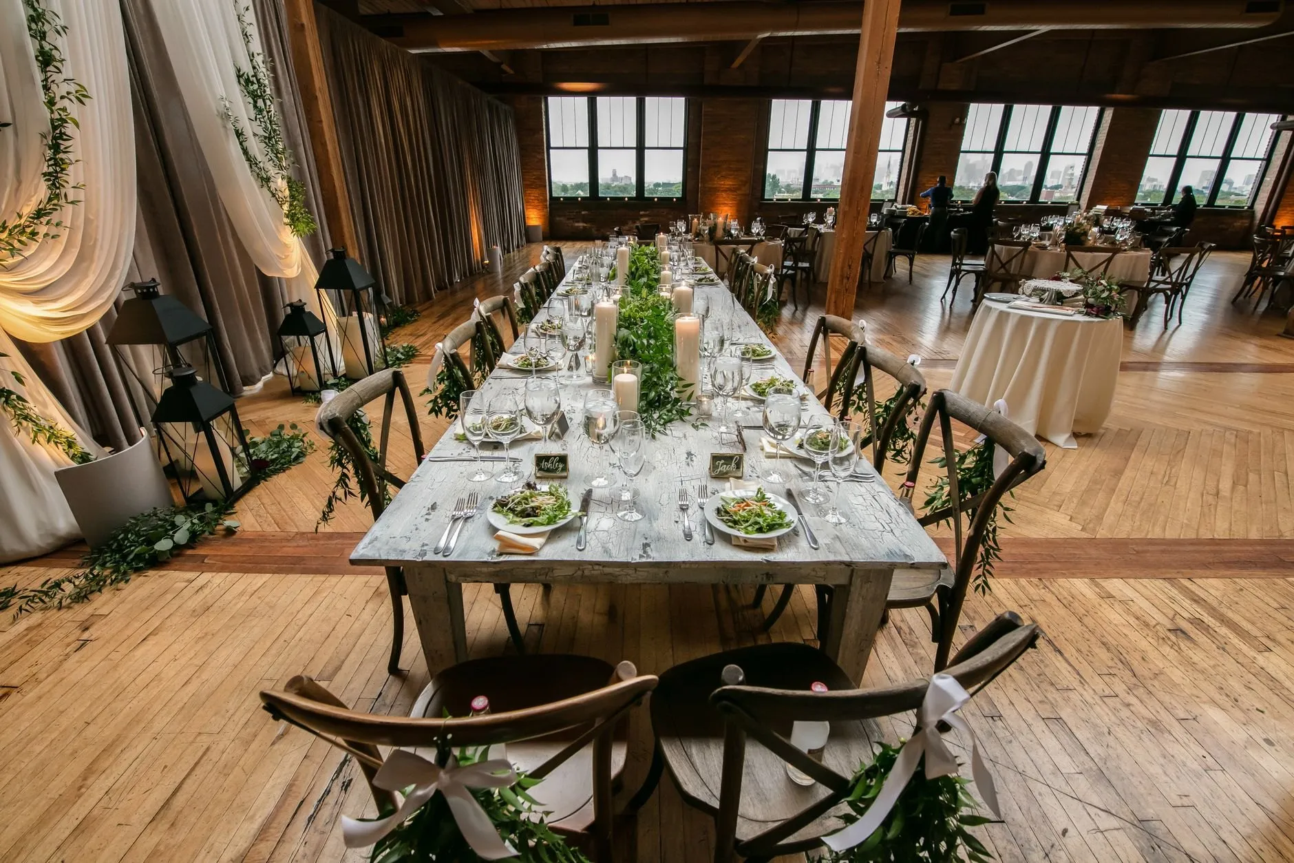 A long table with candles and greenery in a timber-floored loft with tall windows