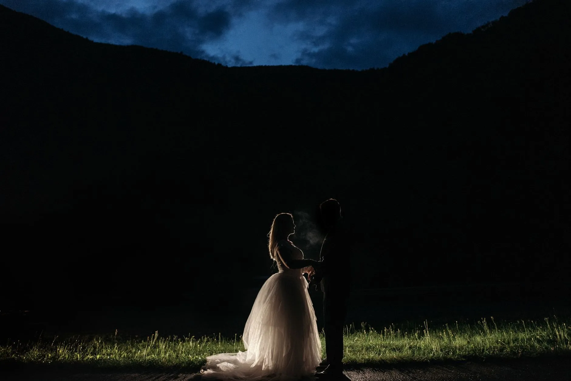 A couple in silhouette at dusk, holding hands in front of dark hills